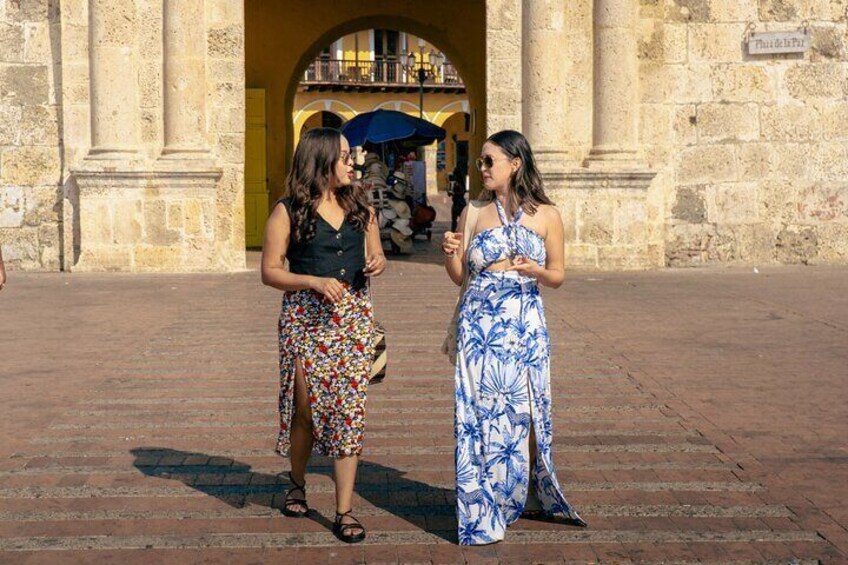 Two women standing on a paved area in front of a stone building with arches. 4