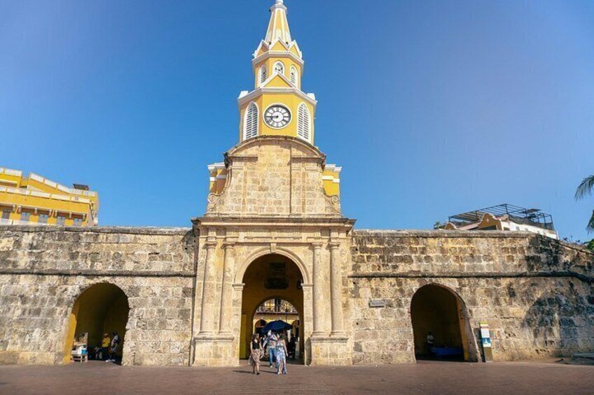 Un edificio storico in pietra con una torre dell'orologio, portali ad arco e un cielo azzurro limpido. 4