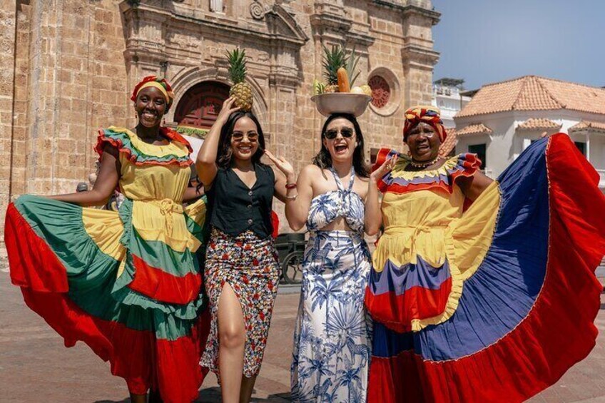 Four people in colorful traditional dresses standing in front of a historic building. 2