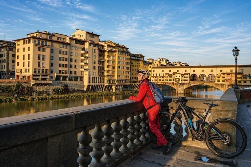 A person in red attire leaning on a railing by a river with a bicycle and a bridge in the background. 5