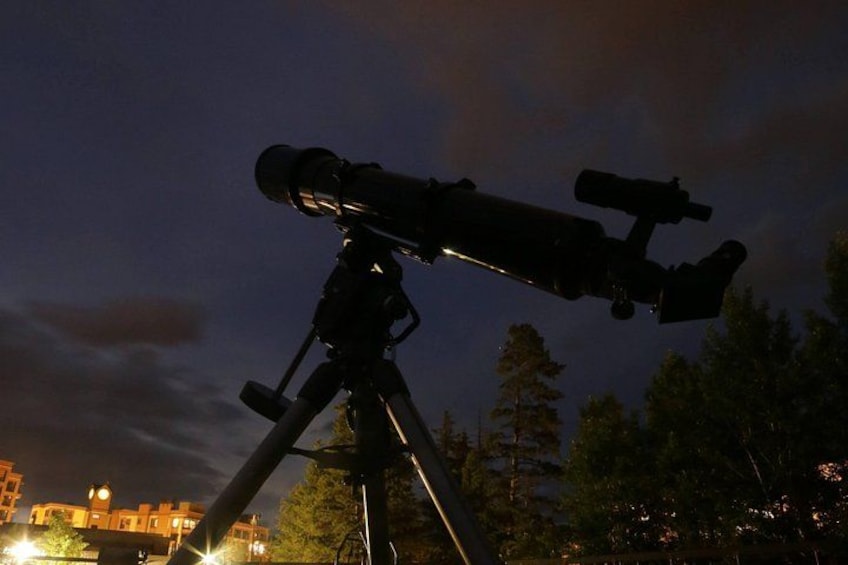 A telescope on a tripod at night with a cityscape in the background. 5