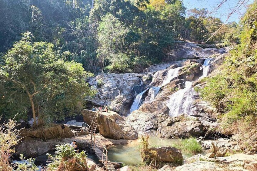 Una cascada que se precipita sobre rocas, rodeada de vegetación exuberante y un pequeño arroyo. 2