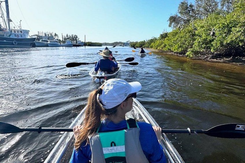 People kayaking on a river with boats in the background. 5