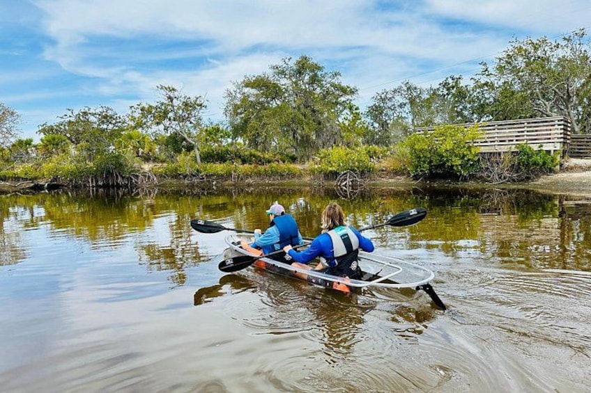 Deux personnes pratiquent le kayak sur une rivière paisible, entourée de verdure. 2