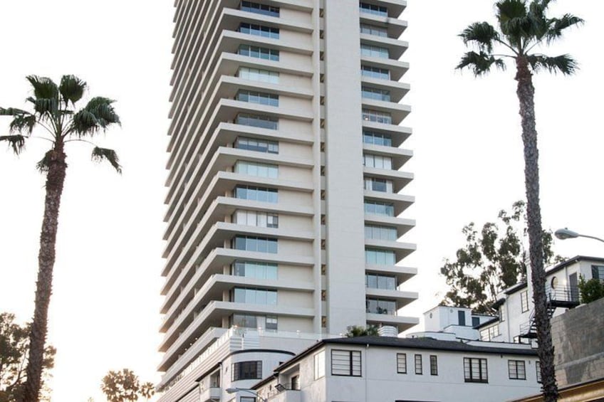 Een hoog wit gebouw met verschillende balkons, omgeven door palmbomen. 3