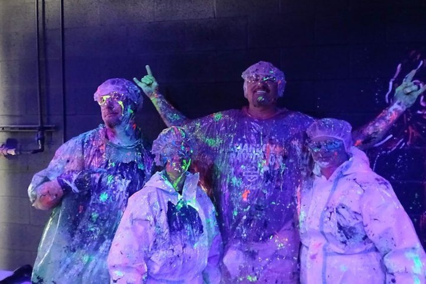 People covered in colorful paint, standing in a dark indoor setting. 1