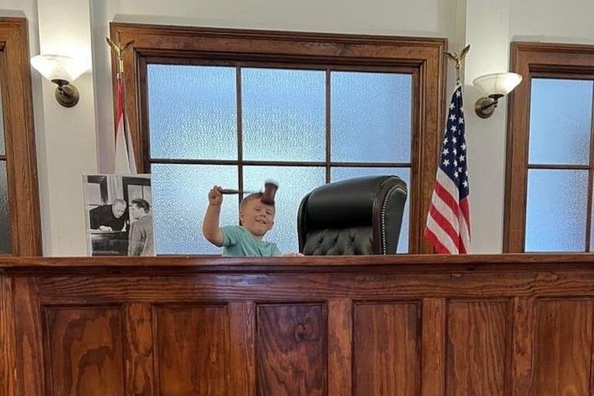 A courtroom with a wooden bench, a black leather chair, and an American flag. 2