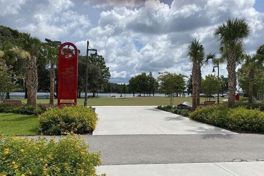 A park entrance with a red sign, palm trees, and a pathway leading to a body of water. 4