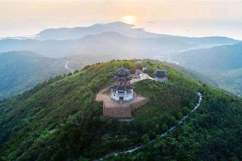 Una pagoda tradizionale su una collina, raggiungibile tramite un sentiero sinuoso, circondata da vegetazione lussureggiante e montagne sullo sfondo. 5
