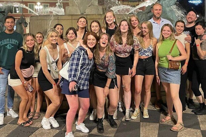 En gruppe mennesker poserer til et foto foran en murstensvæg og et metalhegn i baggrunden. 4