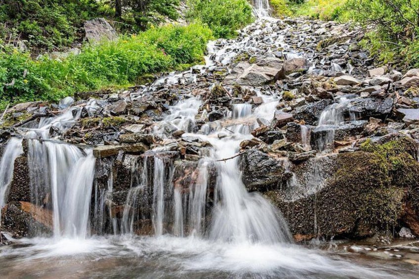 A multi-tiered waterfall cascading over rocks in a forested area. 2