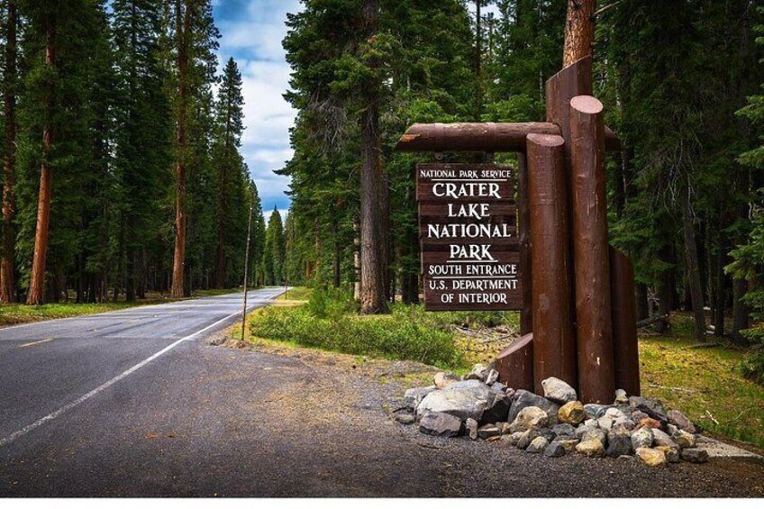 A road leading to Crater Lake National Park with a sign indicating the South Entrance. 5
