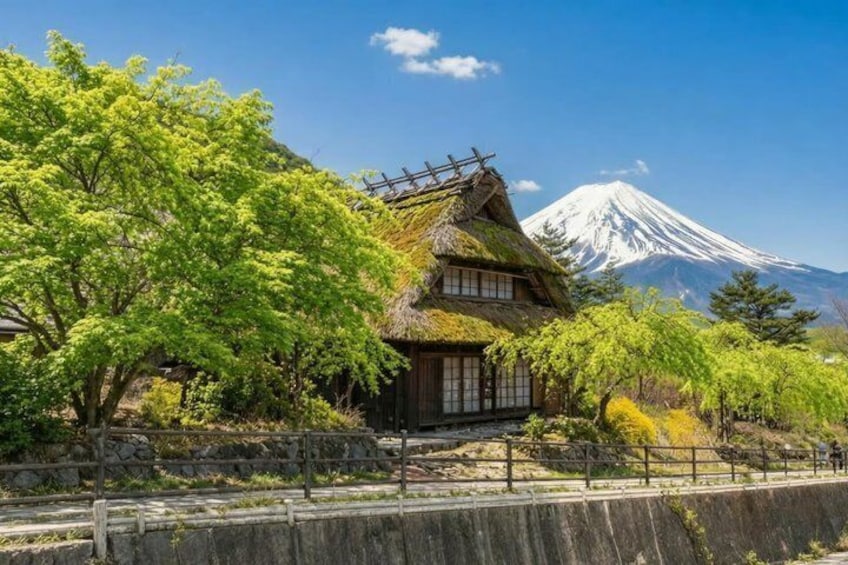 A traditional Japanese house with a thatched roof, a stone wall, and a view of Mount Fuji in the background. 1