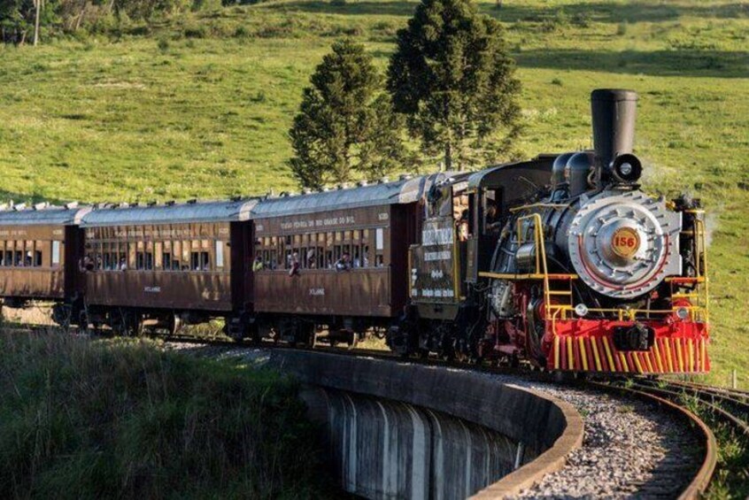 A steam locomotive pulling passenger cars on a curved track through a grassy landscape. 1