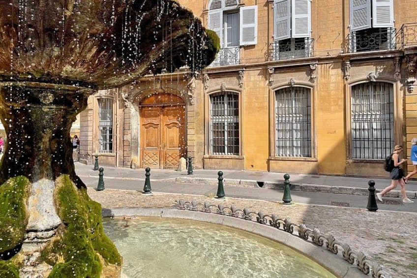 A fountain, a building with a wooden door, and a street with pedestrians. 2
