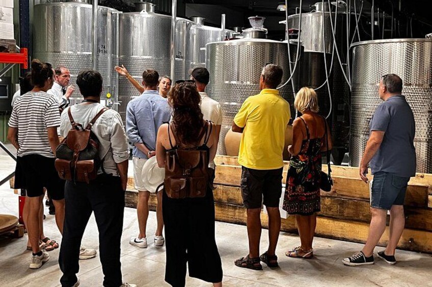 People standing in front of large stainless steel tanks, likely in an industrial or brewery setting. 3