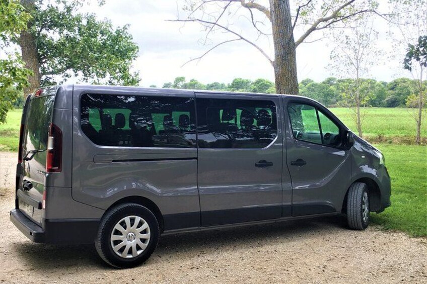 Una camioneta gris estacionada sobre un camino de grava, con árboles y césped al fondo. 3