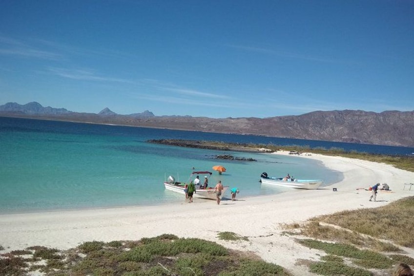 Een strand met boten, mensen en bergen op de achtergrond. 2
