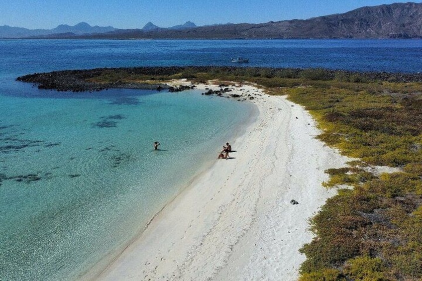Een strand met helder turquoise water, een zandstrand en verre bergen. 1