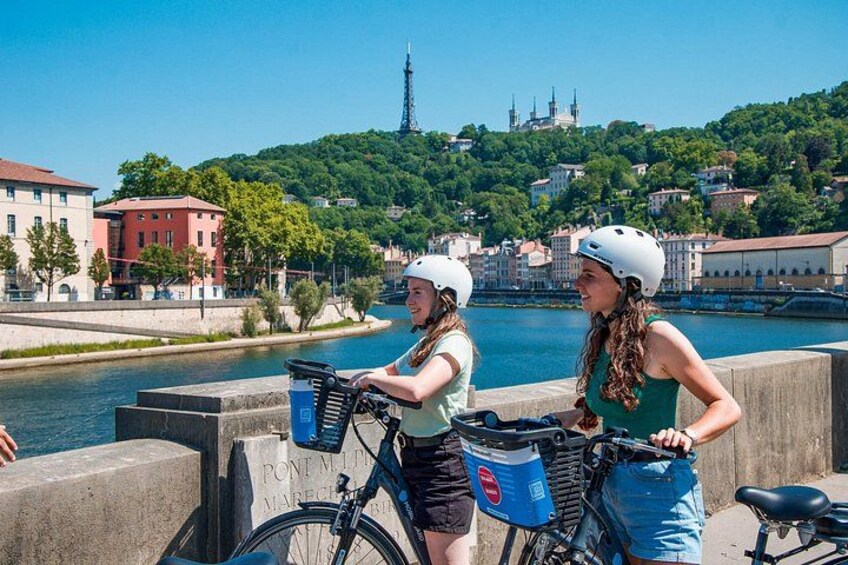 To personer på cykler med cykelhjelme, en flod og en bro i baggrunden. 2