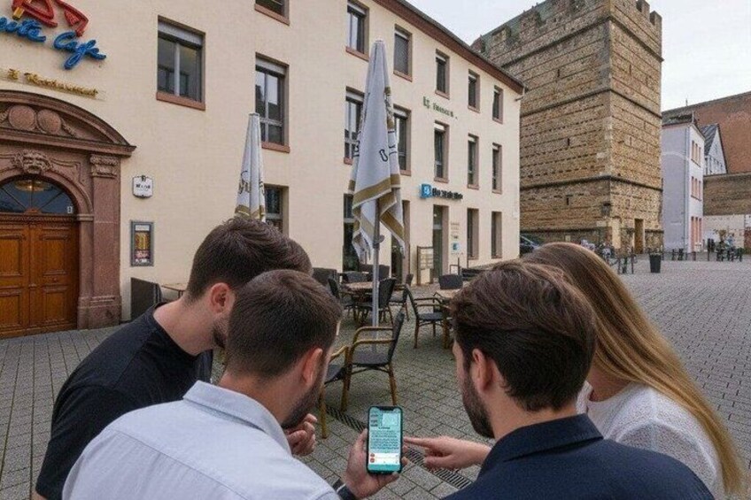 A group of people looking at a smartphone, standing in front of a building with a sign that reads 'Hotel.' 3