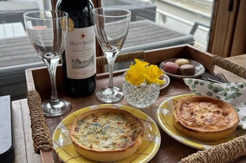 A table with a bottle of Haut Boutet Côtes de Provence wine, two glasses, a tart, a quiche, and macarons. 3