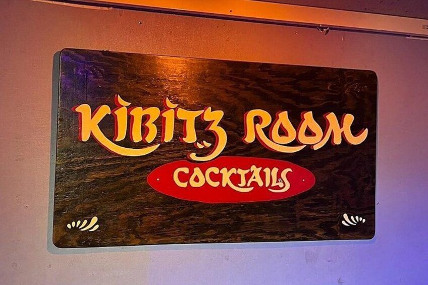 A wooden sign with the text 'KIBITZ ROOM COCKTAILS' in stylized lettering. 3
