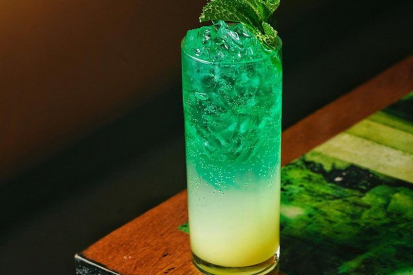 A tall glass with a gradient of green to yellow liquid, ice cubes, and a mint garnish. 4