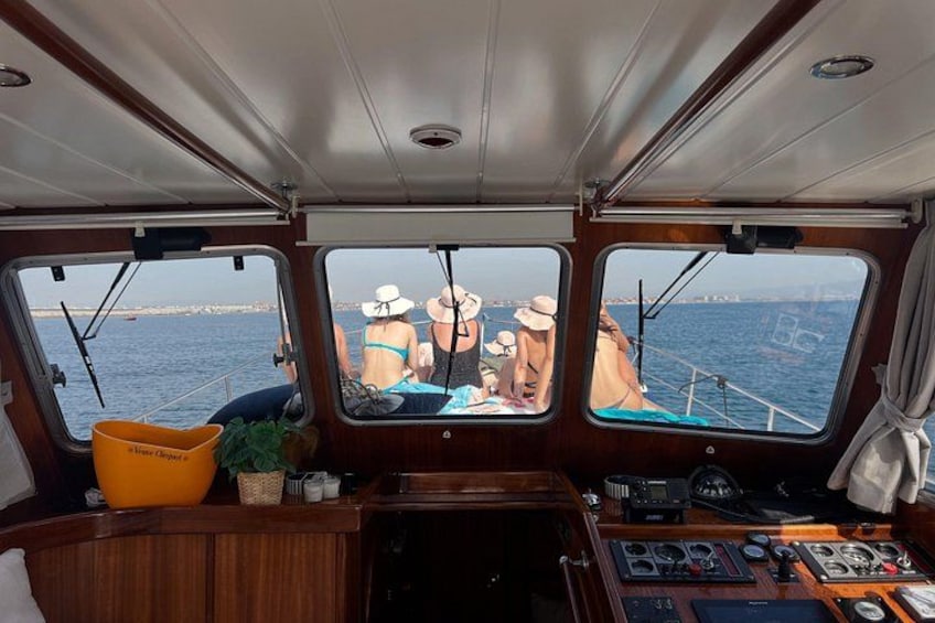 Interior de un barco con timón, panel de control y ventanas con vistas al mar. 2