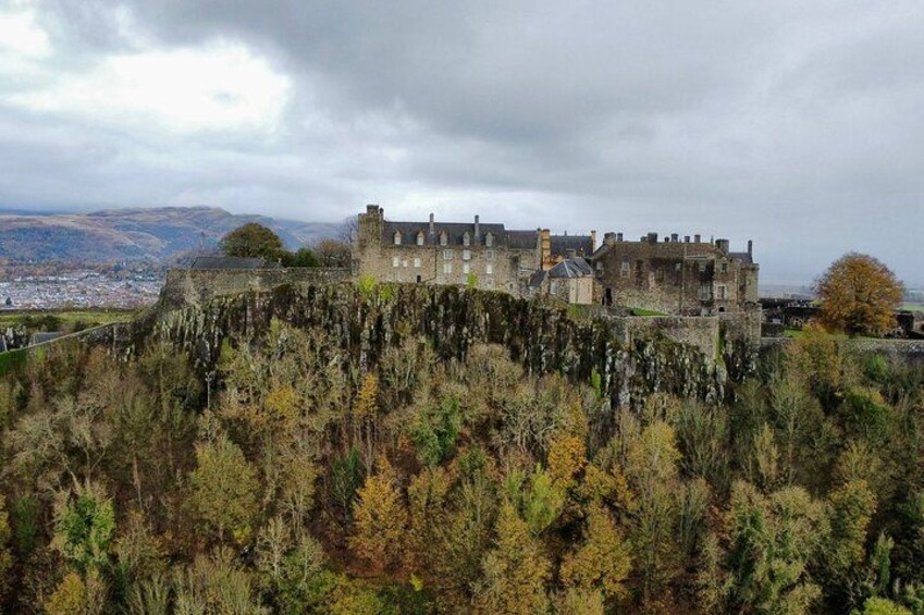 A historic castle on a hill with autumn foliage, overlooking a distant town. 2