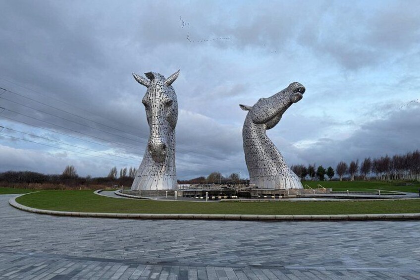 The Kelpies, two large horse sculptures, in a landscaped area with a paved walkway. 3