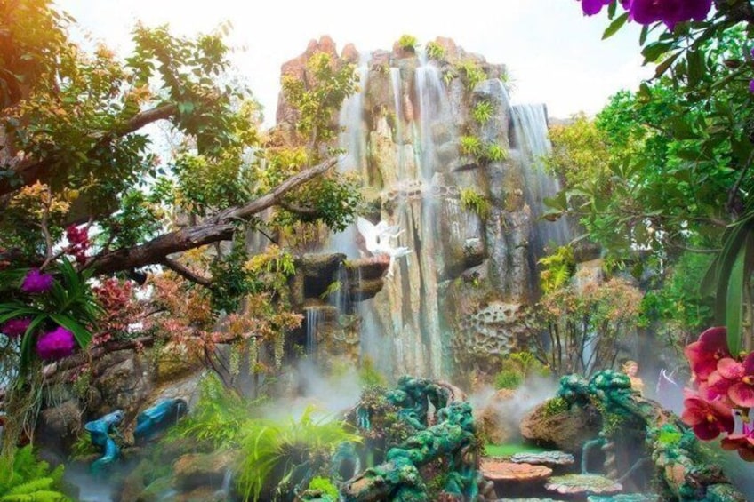 Una cascata che si getta da una scogliera rocciosa, circondata da vegetazione rigogliosa e piante fiorite. 3