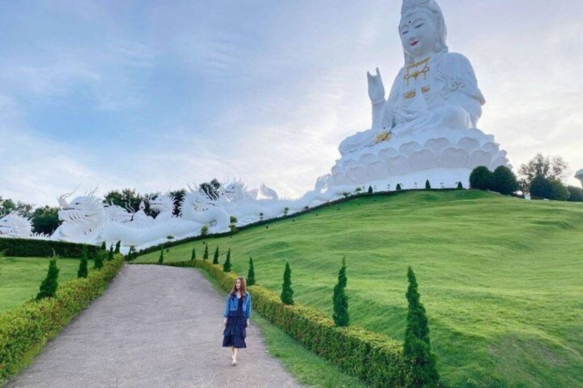 Un'imponente statua bianca raffigura una figura seduta su una collina, con un sentiero che vi conduce e sculture di draghi bianchi lungo il percorso. 5