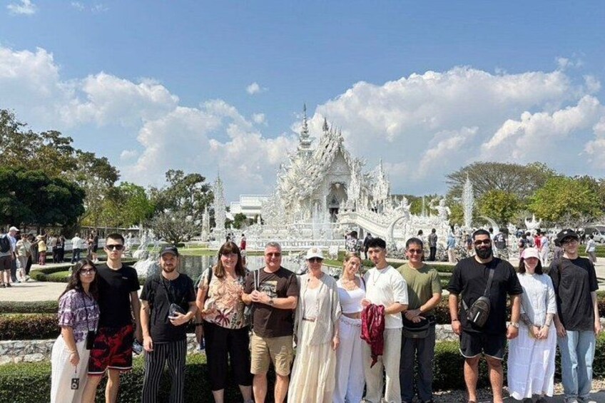 A group of people standing in front of a white ornate temple with a fountain. 2
