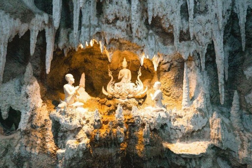 Eine Höhle mit einer Buddha-Statue, umgeben von kleineren Figuren, vor einer Kulisse aus Stalaktiten. 4
