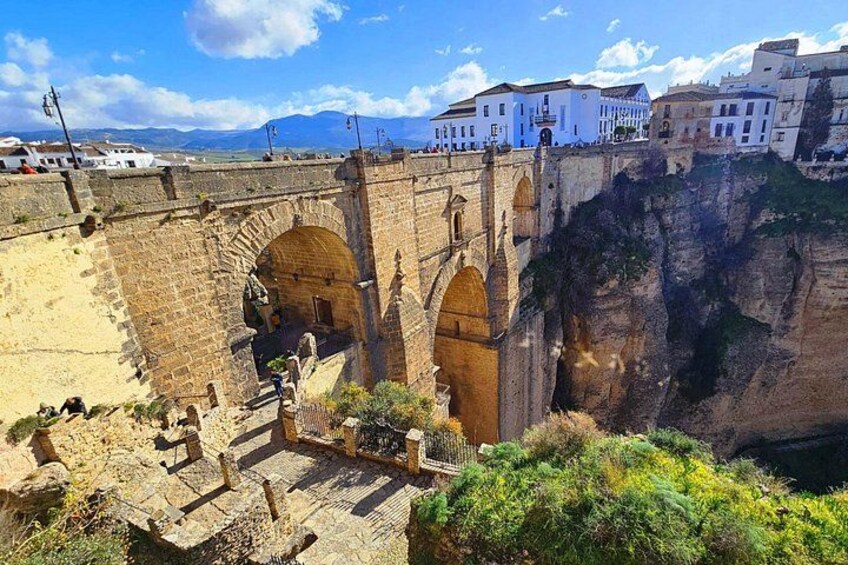 A stone bridge with arches, a cliffside, and buildings in the background. 3
