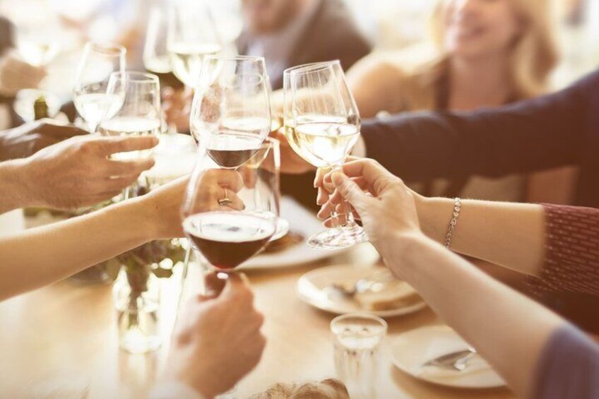 Een groep mensen die met wijnglazen proosten aan een tafel. 2