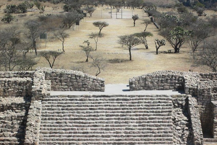 Ruinas antiguas de piedra con estructuras escalonadas y un paisaje árido con escasos árboles. 4