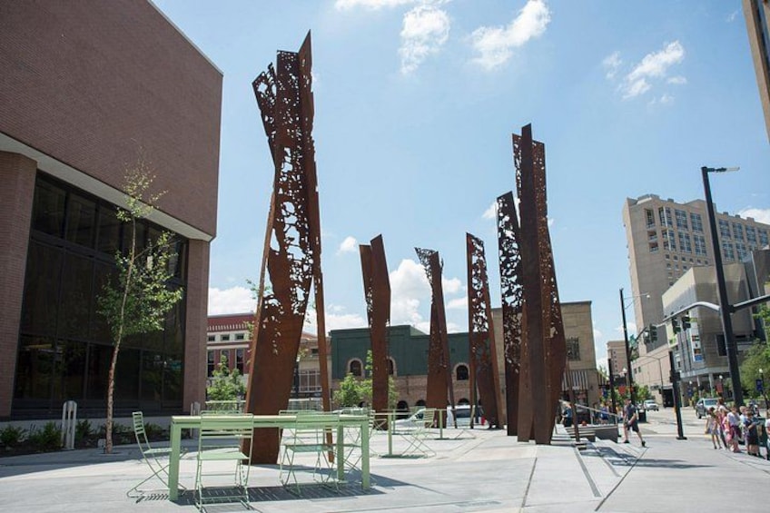 A public square with a green metal table and chairs, surrounded by tall, rust-colored sculptures. 2