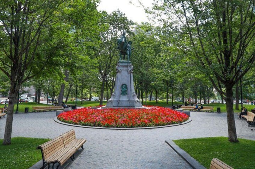 A park with a central monument, benches, and a flower bed. 4