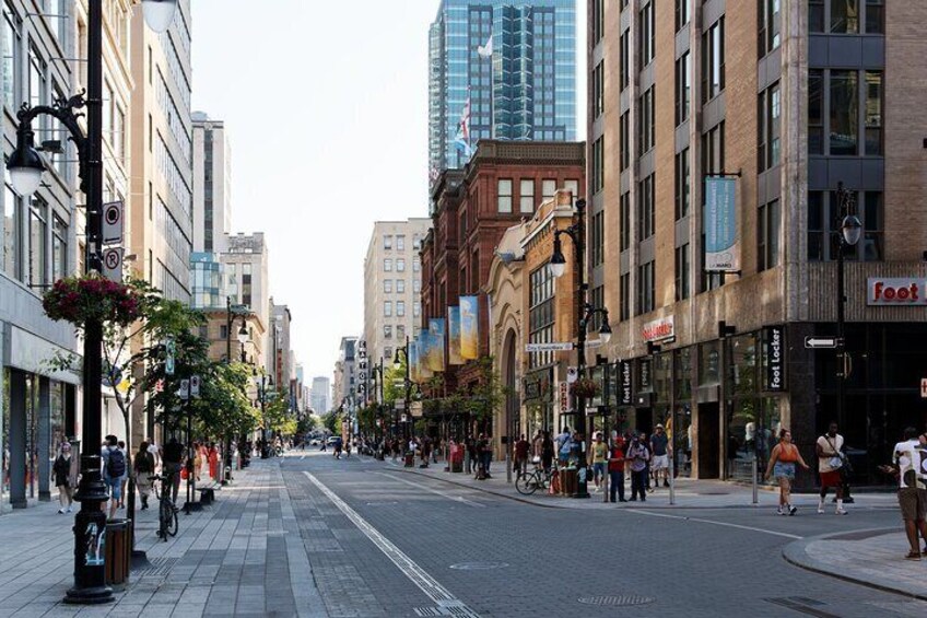 A city street lined with buildings, including a Foot Locker store, and a cyclist on the sidewalk. 5