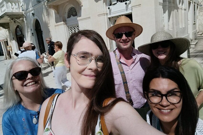 A group of people taking a selfie in front of a historic building with arches and columns. 2