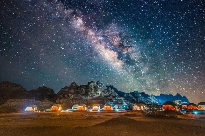 Cielo estrellado con la Vía Láctea, una cadena montañosa y tiendas de campaña iluminadas. 4