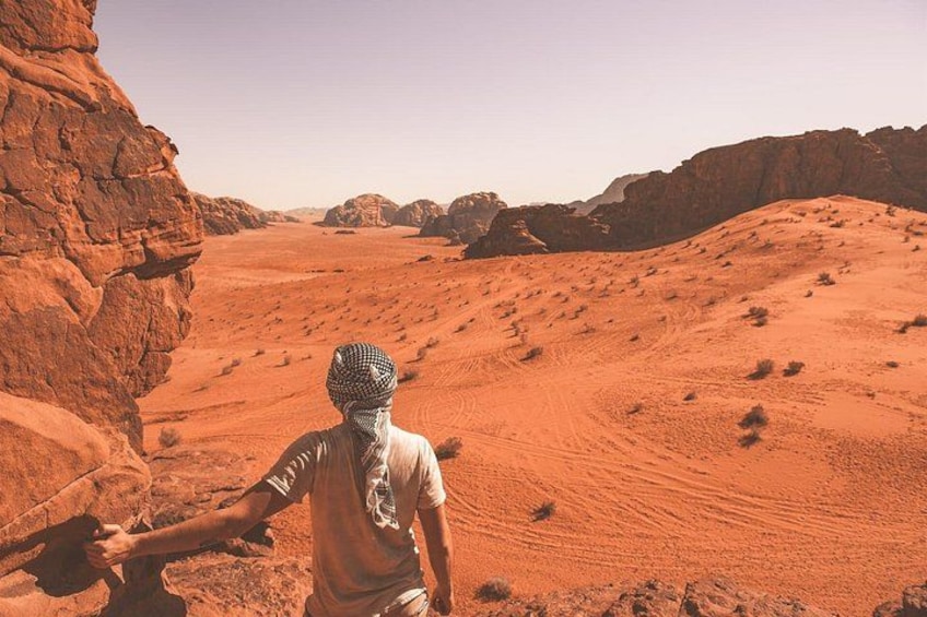 Una persona de pie en un desierto con arena roja y terreno rocoso. 3