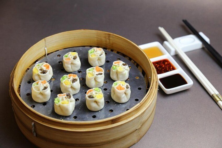 A bamboo steamer with dumplings, chopsticks, and dipping sauces. 5