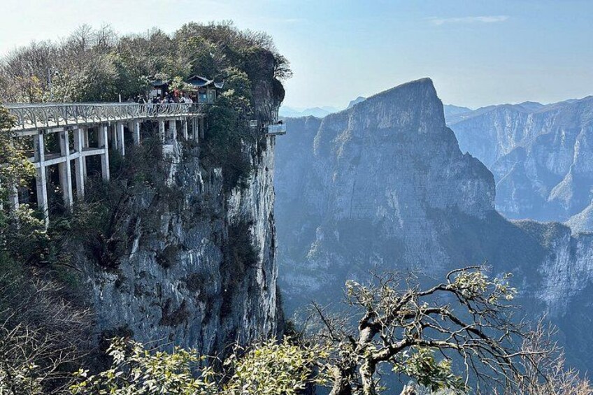 A narrow bridge over a steep cliff, with a mountainous landscape in the background. 5