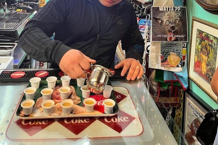 A person pouring a beverage into a cup on a tray with multiple cups. 3