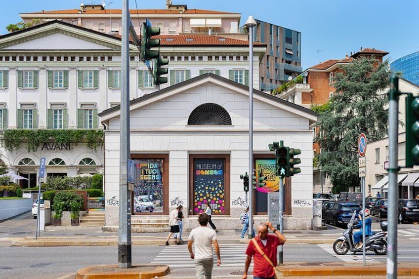 A street scene with a building that has a classical facade, a pedestrian crossing, traffic lights, and a parked motorcycle. 4