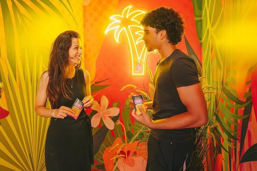 Deux personnes tenant des produits devant un décor coloré, sur le thème des tropiques, avec des palmiers et des fleurs. 2