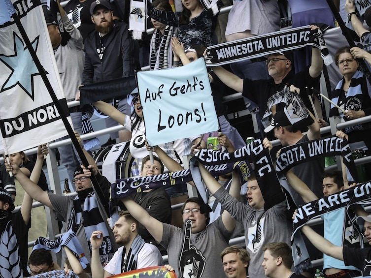 A crowd of fans at a sporting event, holding banners and flags, with one banner reading 'Ave Gents Loons!' 4